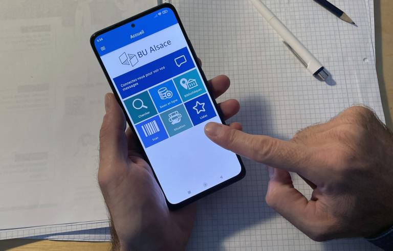 Des mains qui tiennent un smartphone avec ouvert l'application BU Alsace